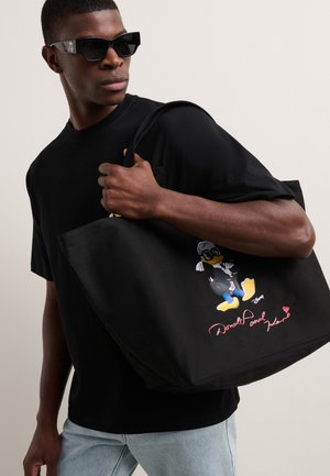 Borsa a tracolla in tela nera con design di un personaggio dei cartoni animati di Paperino in giacca, con vivaci accenti gialli e dettagli rosa della firma.
