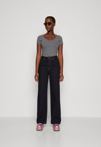 Camiseta de manga corta a rayas, jeans oscuros de cintura alta y zapatos de plataforma rosa brillantes, con gafas de sol negras y pendientes de aro.