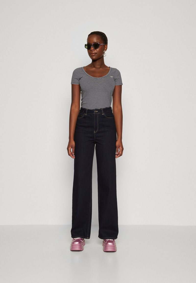 Camiseta de manga corta a rayas, jeans oscuros de cintura alta y zapatos de plataforma rosa brillantes, con gafas de sol negras y pendientes de aro.
