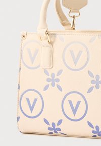 Borsa a mano in pelle beige con motivi floreali e cerchi blu contenenti la lettera V, dotata di manico curvo e accessori in metallo dorato.
