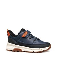 Zapatilla deportiva en azul marino y negro con suela blanca gruesa, detalles en naranja, correa de velcro y cordones elásticos, diseñada para un uso casual.
