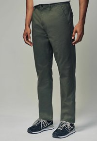 Grønne bomuldsblandede chinos med lige ben, knaplukning og sidelommer, parret med sorte sneakers og grå snørebånd.