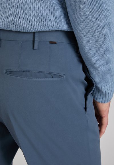 Hellblauer Strickpullover kombiniert mit dunkelblauer Hose mit einer Gesäßtasche und glattem, strukturiertem Stoff. Dezente Nahtdetails sichtbar.