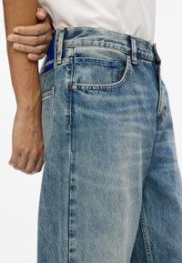 Gai zilas džinsi ar taisnu piegriezumu. Raksturīgas iezīmes: pogu un rāvējslēdzēja aizdare, piecas kabatas un zīmola uzlīme uz jostasvietas.