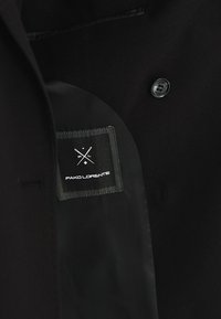 Wnętrze czarnej kurtki o gładkiej teksturze, z metką "Pako Lorente" oraz jednym czarnym guzikiem po prawej stronie.