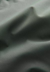 Dunkelgrüner Stoff mit einer glatten, leicht glänzenden Textur, die subtile Falten und Wellen aufweist, die seine leichte Qualität betonen.