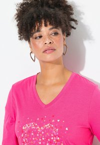 Camiseta de cuello en V rosa con un diseño de corazón compuesto por corazones de confeti multicolor; textura suave y mangas cortas.