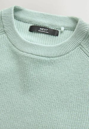 Světle zelený pletený svetr s kulatým výstřihem, který má texturované žebrování. Černá nálepka značky "NEXT", vyrobena v Bangladéši.