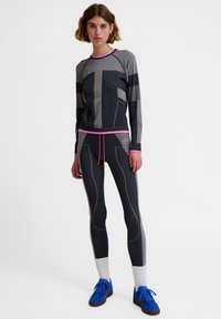 Zestaw sportowy składający się z dopasowanej, długorękawowej bluzy w kolorze szarym z różowymi akcentami, w komplecie z dopasowanymi leginsami i niebieskimi butami sportowymi. Tkanina o fakturze.