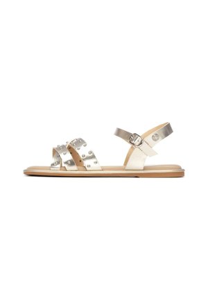 Sandalias doradas metálicas con tres tiras cruzadas decoradas con tachuelas y una correa en el tobillo con hebilla. Suela plana con acentos en beige claro.