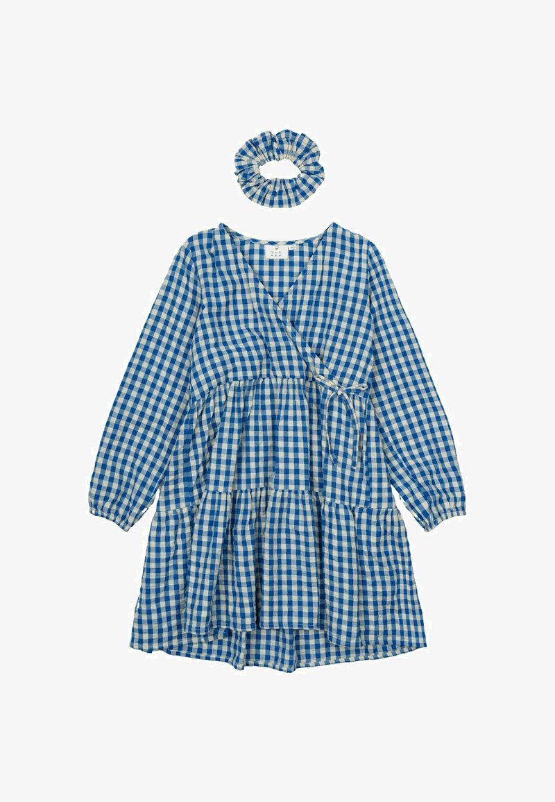 Robe portefeuille en vichy bleu et blanc avec des manches longues, design à volants, et un chouchou assorti. Présente un décolleté en V et un détail de taille à nouer.