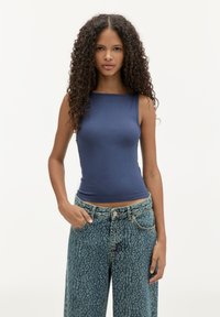 Mørkeblå tætsiddende ærmeløs top lavet af blødt stof, parret med højtaljede, lyse teal jeans med leopardmønster.