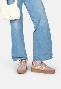Sneaker con una toma superiore in suede marrone chiaro, accenti beige, punta rotonda e una spessa suola piattaforma marrone; abbinati a jeans a gamba larga blu sbiaditi e una borsa bianca intrecciata.