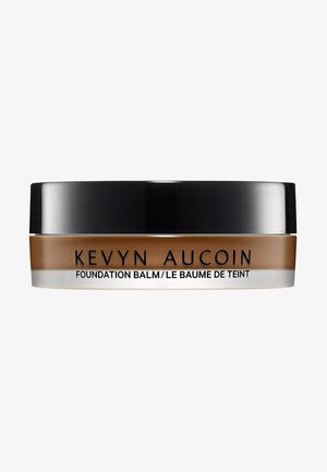 Foundation-Balsam in einem runden Behälter mit einem schwarzen Deckel und einer klaren Basis. Das Etikett zeigt "Kevyn Aucoin" und Produktinformationen in schwarzer Schrift.