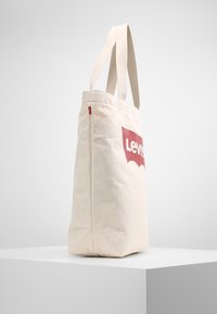 Linned tote-väska i off-white färg, med röd Levi's-logga på framsidan. Dubbla tyghandtag; rektangulär form med slät yta.