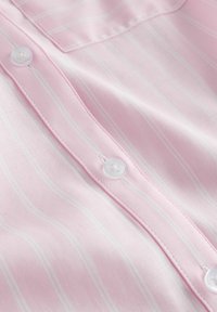 Gaiši rozā kokvilnas krekls ar smalkām baltām vertikālām svītrām, baltām pogām un detalizētām šuvēm gar pogu līniju.