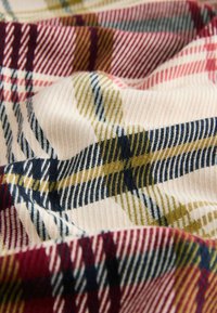Checkered fabric in cream, featuring patterns in red, navy, green, and beige, with a ribbed texture that adds depth to the design.