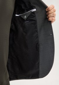 Schwarzes Innenfutter einer Jacke mit geometrischem Muster. Grauer Außenstoff mit glatter Textur und weißen Nähten entlang der Nähte.