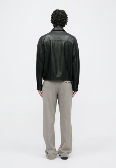 Μαύρο δερμάτινο μπουφάν με γιακά και μακριά μανίκια, συνδυασμένο με ανοιχτό γκρι, πτυχωτούς παντελόνες. Λείο υλικό, απλός σχεδιασμός.