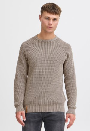 Knit sweater in light brown with textured pattern, ribbed cuffs, and hem. Features a crew neckline and a label on the side.