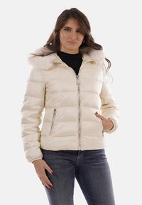 Giacca da donna bianca imbottita con cappuccio foderato in pelliccia, cerniera frontale e tasche laterali; presenta una texture liscia e cuciture orizzontali.