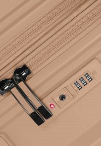 Beige Hartschalenkoffer mit schwarzen Reißverschlüssen, doppelten Reißverschluss-Ziehern und einem von der TSA genehmigten Schloss. Verfügt über eine strukturierte Oberfläche mit einem dezenten Muster.