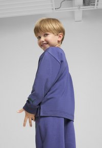 Sudadera morada y pantalones a juego, hechos de material suave, con bordado del logo verde de Puma en la manga y el costado.