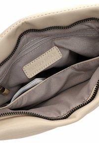 Interno della borsa beige con una texture liscia, dotato di una tasca con cerniera, rivestimento in tessuto e un'etichetta impressa con "EMILY & NOAH."