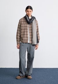 Bruin geruit flanellen overhemd, grijze sjaal, wit shirt, grijze wijde broek en bruine schoenen; minimalistisch ontwerp met zachte texturen.