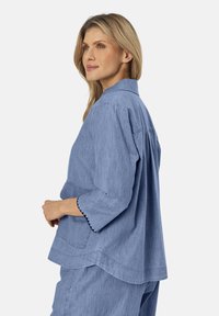 Blusa di chambray azzurro chiaro con maniche a tre quarti, design colletto e dettagli smerlati sui bordi manica. Offre una vestibilità comoda.