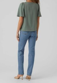 Top verde a maniche corte con retro quadrato, abbinato a jeans dritti azzurri chiari e scarpe con tacco nudo. Tessuto dalla superficie liscia.