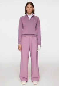 Lila zip-up sportstopp med långa ärmar, matchad med löst sittande byxor. Vita detaljer och golfhandske fulländar outfiten.