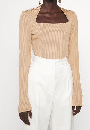 Beżowy prążkowany top z długim rękawem o kwadratowym dekolcie; dopasowany krój z dzwonkowatymi rękawami. Połączony z białymi spodniami z wysokim stanem.