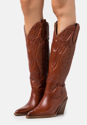 Botas de vaquero de cuero marrón con puntas puntiagudas, costuras intrincadas y cañas altas y anguladas. Diseño con tacón y detalles decorativos.