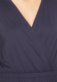 Granatowa bluzka o kroju kopertowym, wykonana z miękkiego materiału, z głębokim dekoltem w kształcie V, marszczoną talią i subtelną teksturą. Gładkie wykończenie z starannymi szwami.
