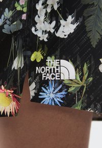 Svart stoff med fargerik blomstermønster og hvit The North Face-logo plassert over bare hud.