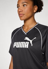 Maillot de sport noir à manches courtes, avec des accents blancs et un grand logo Puma blanc sur le devant. Design en V, texture lisse.