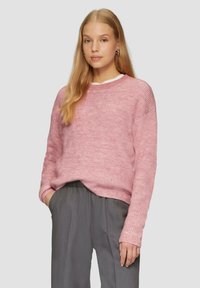 Helles rosa Strickpullover mit entspannter Passform, geripptem Muster und langen Ärmeln. Kombiniert mit lockeren grauen Hosen.