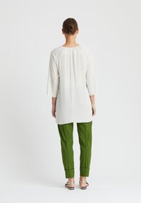 Weiße langärmlige Bluse mit rundem Halsausschnitt, kombiniert mit enganliegenden grünen Hosen, die umgeschlagene Manschetten und Sandalen mit silberner Schnalle aufweisen.