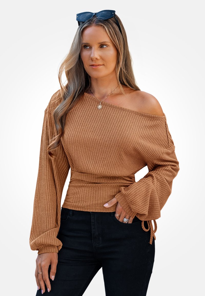 Pasiasty, brązowy top typu off-the-shoulder z długimi, rozszerzanymi rękawami i dopasowanym talią. Połączony z czarnymi spodniami i warstwowymi dodatkami biżuteryjnymi.