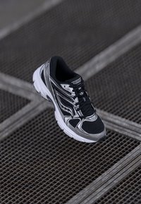 Black and silver running shoe with a mesh upper, textured detailing, and a cushioned sole, featuring black laces and logo embossed on the tongue.