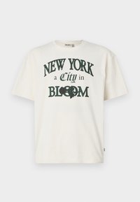 Kræmfarvet bomulds t-shirt med korte ærmer, med et trykt design der siger "NEW YORK en By i BLOOM" i mørkegrøn.