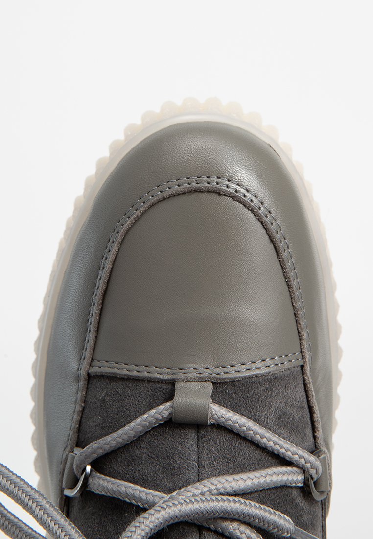 Szare trampki z gładką skórzaną osłoną na palce, miękkim zamszowym korpusem, teksturowanymi sznurowadłami i przezroczystą podeszwą z ząbkowanym wykończeniem.