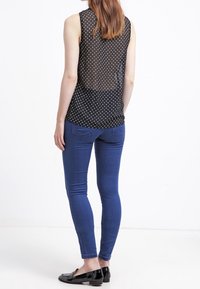 Top negro sin mangas con lunares blancos, tejido transparente en la parte de atrás, combinado con jeans ajustados azules y bailarinas negras.