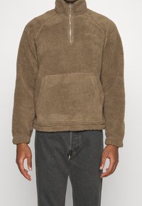Brauner Fleece-Pullover mit hohem Kragen, halbem Reißverschluss und Vordertasche. Strukturierter, gemütlicher Stoff; entspannte Passform.