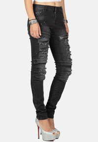 Jean skinny noir avec des détails déchirés, quincaillerie argentée et design ajusté. Portés avec des chaussures à plateforme à talons hauts argentées.