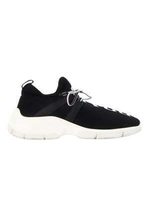 Sort sneakers med tyk hvid sål, hvid tekst på toppen, strikket stof og snørelukning med en løkke ved hælen.