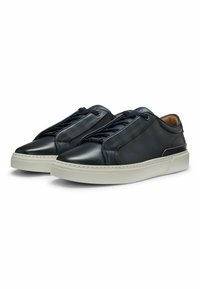 Nahkaiset tennarit tummansinisinä, joissa on sileä pinta, slip-on-malli ja tummat nauhat, asetettu valkoiselle kumipohjalle, jossa on minimaalista korostusta.
