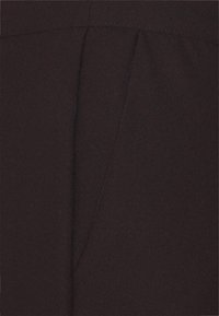 Bruine stof met een zachte textuur en een geplooid ontwerp. Zomen zijn zichtbaar, wat een gestructureerde uitstraling creëert.