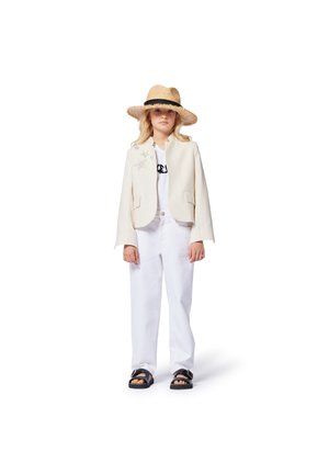 Veste blanche avec des accents d'étoiles argentées, t-shirt blanc, pantalon blanc ample et sandales noires. Le modèle porte un chapeau en paille à large bord.